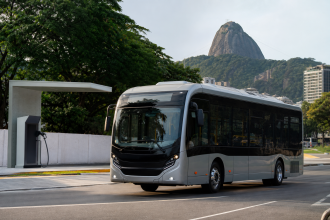 Ônibus elétrico urbano circula no Rio de Janeiro próximo a uma estrutura de transporte público.