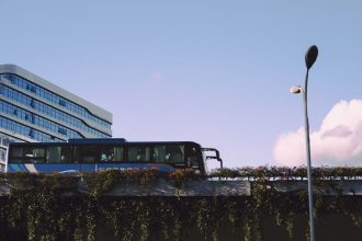 Ônibus moderno circula diante de um edifício envidraçado em uma área urbana.