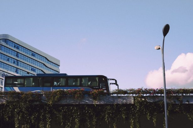 Ônibus moderno circula diante de um edifício envidraçado em uma área urbana.