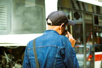 Homem examina um ônibus quebrado parado em uma rua urbana.