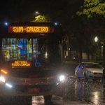 Ônibus urbano circula à noite sob chuva em uma via de Belo Horizonte.