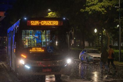 Ônibus urbano circula à noite sob chuva em uma via de Belo Horizonte.